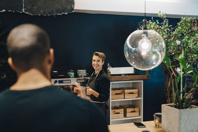 Smiling female owner looking at male customer in cafeteria