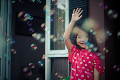 Portrait of smiling girl with arm raised seen through bubbles