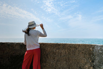 Rear view of woman standing at beach against sky