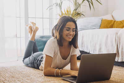 Smiling girl lying on floor while using laptop at home