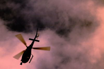 Low angle view of helicopter flying in cloudy sky at dusk