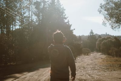 Rear view of man standing by trees against sky