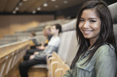 Portrait of happy young woman sitting in auditorium with friends in background