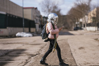 Girl with space helmet using mobile phone while walking on road