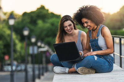 Happy young woman using phone while sitting on laptop