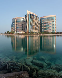 Reflection of buildings in lake against clear blue sky