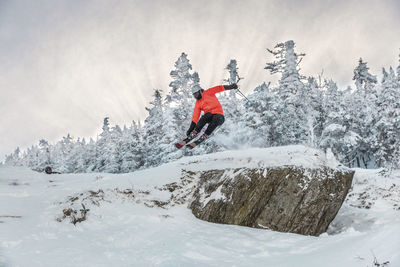 Full length of man doing stunt while skiing on snow against trees during winter