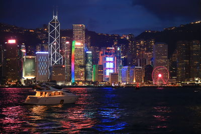 Illuminated buildings by sea against sky at night