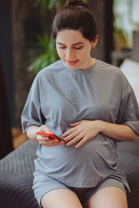 Young woman using mobile phone while sitting on bed at home