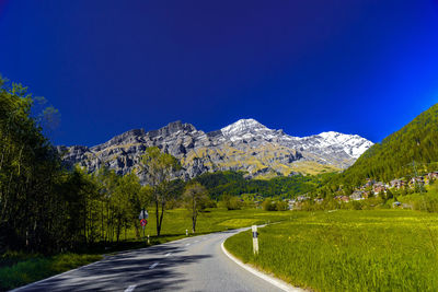 Road leading towards mountains against clear blue sky