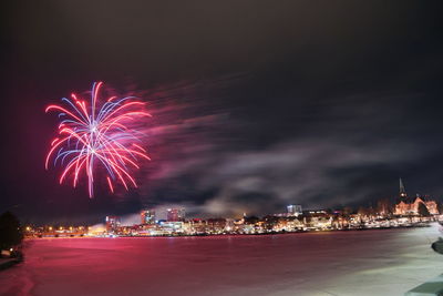 Firework display over illuminated city against sky at night