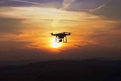 Low angle view of silhouette drone against dramatic sky during sunset