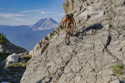 Hiker riding bicycle on mountain against sky