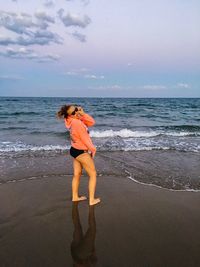 Side view of playful woman standing on shore against sky