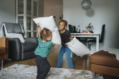 Sisters play-fighting with pillows at home