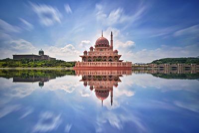 Mosque reflecting in lake against blue sky