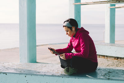 Woman using mobile phone while sitting by sea