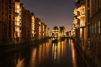 Canal amidst illuminated buildings in city at night