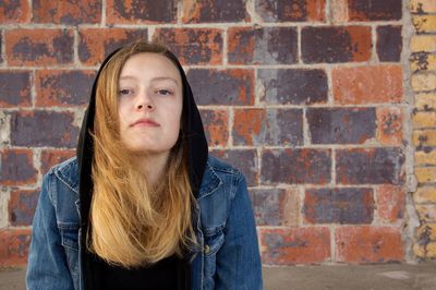 Portrait of young woman against brick wall