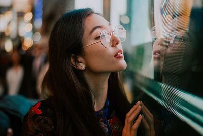 Close-up of young woman standing against illuminated city at night