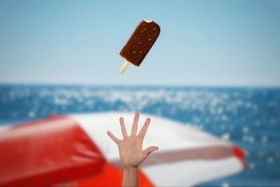 Cropped image of hand catching ice cream against sea