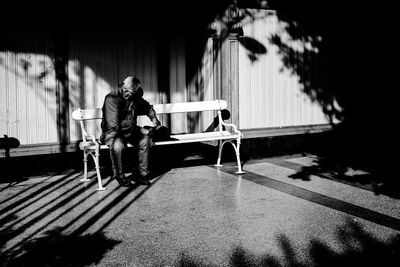 Full length of man sitting on bench during sunny day