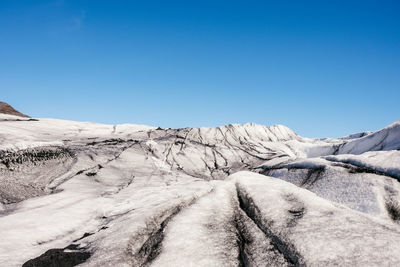 Snow covered landscape against clear blue sky