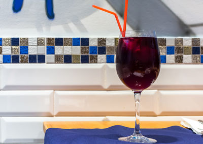 Full glass of deep red sangria wine with two red straws on the white tile background