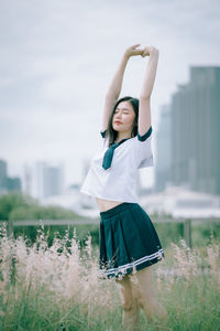 Young woman with arms raised standing amidst plants on field