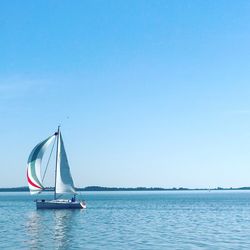 Sailboat sailing in sea against clear blue sky