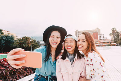 Cheerful young friends taking selfie in city 