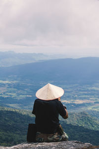 Rear view of man sitting on cliff against mountains