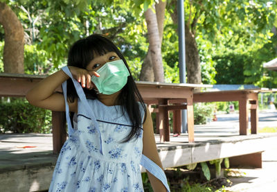 Photo of a little girl wearing a protective facemask to protect dust and virus standing in a park.