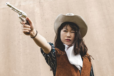 Young woman aiming gun while standing against wall