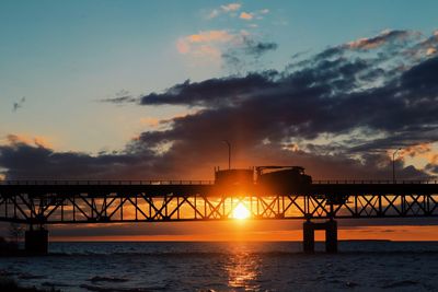 Silhouette bridge over sea against sky during sunset