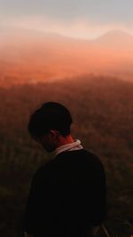 Rear view of man standing against landscape during sunset