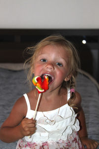 Portrait of cute girl eating lollipop while sitting on bed