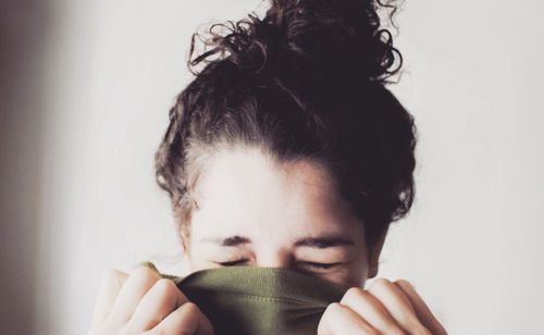 Close-up of woman covering face with fabric against white wall