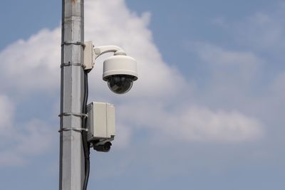 Low angle view of security camera against cloudy sky during sunny day