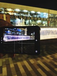 Man photographing illuminated smart phone on floor in city at night