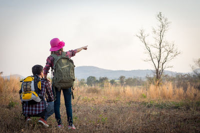 Rear view of couple with backpacks on grassy field against sky