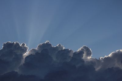 Low angle view of sunlight streaming through clouds