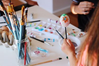 Cropped image of girl holding painted eggshell at table