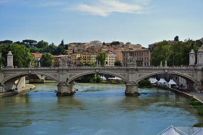 Arch bridge over river in city against sky