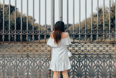 Rear view of woman standing by chainlink fence