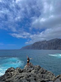 Rear view of man standing on rock by sea against sky