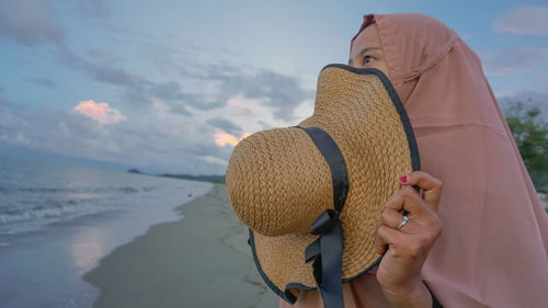 Midsection of woman holding hat against sky during winter