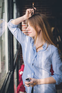 Young woman looking through window holding paintbrush