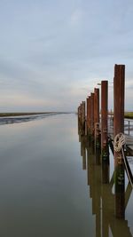 Wooden posts in sea against sky