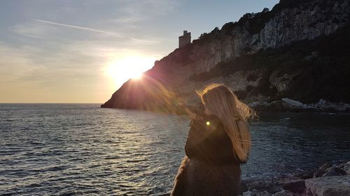 Woman standing on rock by sea against sky during sunset